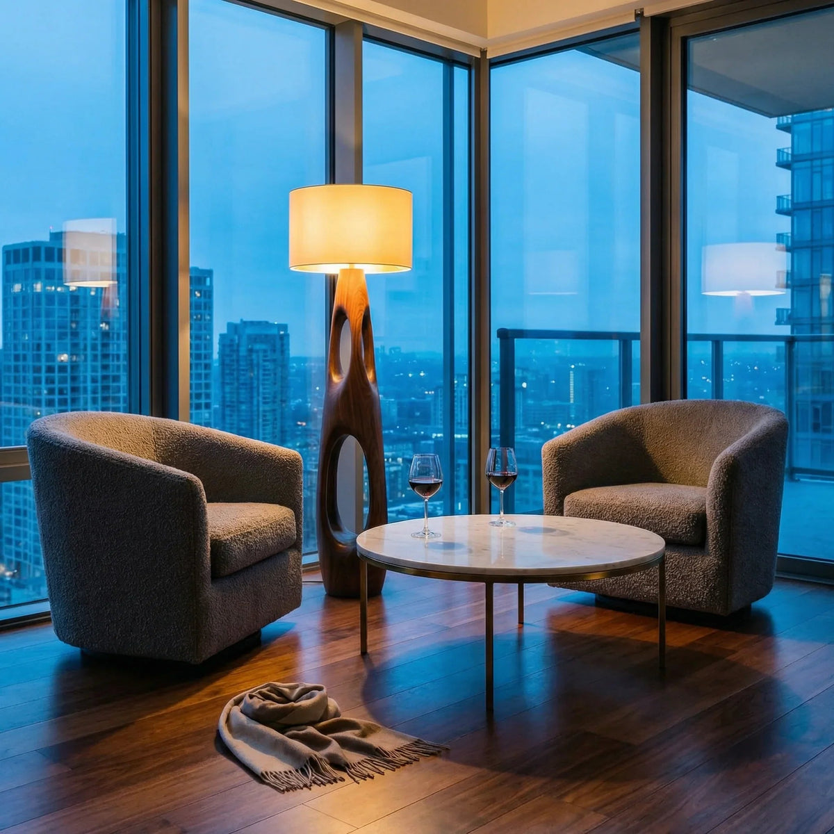 Modern carved wood floor lamp with dual openings beside two armchairs and round table in a city view living room