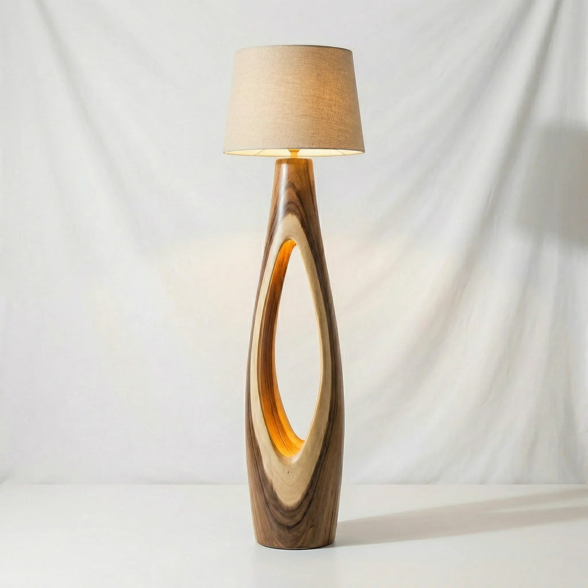 Modern floor lamp with oval-shaped, solid wood base and beige fabric shade on white backdrop